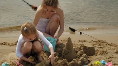 Anne ve kızı sahilde kumdan bir kale inşa oynuyorlar. Yaz güneşli bir gün. Tatil