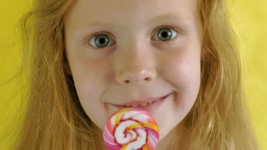 Sarı arka planda lolipopu olan küçük bir kız. Portreyi kapat