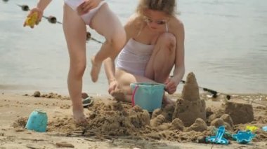 Anne ve kızı sahilde kumdan bir kale inşa oynuyorlar. Yaz güneşli bir gün. Tatil
