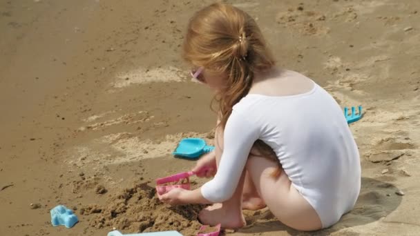 Ragazza bambino gioca con la sabbia sulla spiaggia utilizzando statuette stampi. Giornata estiva soleggiata. vacanza — Video Stock