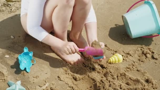 Niña juega con arena en la playa usando figuras de moldes. Día soleado de verano. vacaciones — Vídeos de Stock