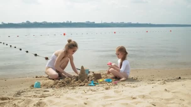 Mutter und Tochter spielen am Strand und bauen eine Sandburg. Sommersonniger Tag. Urlaub — Stockvideo