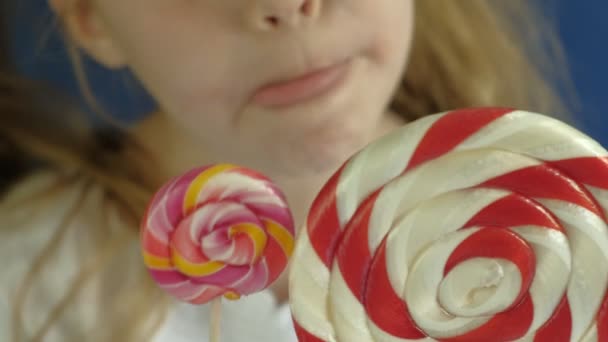 Little girl with a lollipop on a blue background. Close up portrait — Stock Video