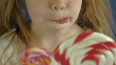 Mavi arka planda lolipopu olan küçük bir kız. Portreyi kapat