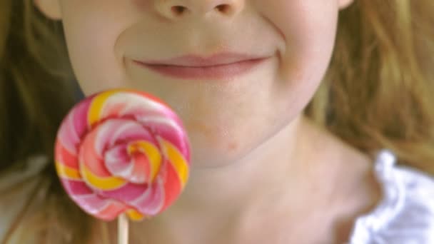 Niña con una piruleta sobre un fondo azul. Primer plano retrato — Vídeo de stock