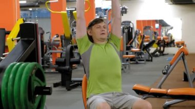 Bir adam bir fitness stüdyosunda düz bir kavrama ile oturan dumbbells ile bir bank basın yapıyor