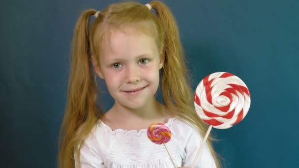 Klein meisje met een lolly op een blauwe achtergrond. Close-up staand — Stockvideo