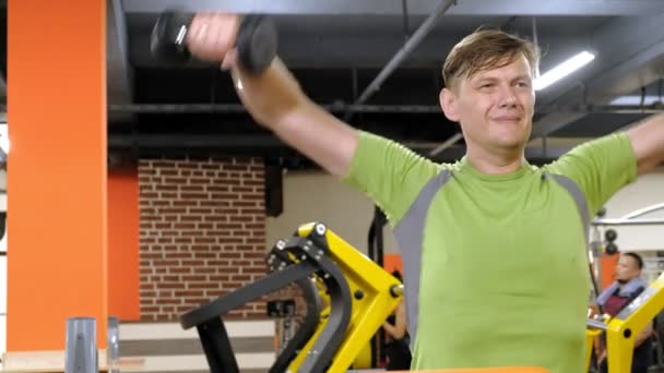 Een man doet een oefening op de rug Delta met dumbbells zittend met een rechte greep in een fitness studio — Stockvideo