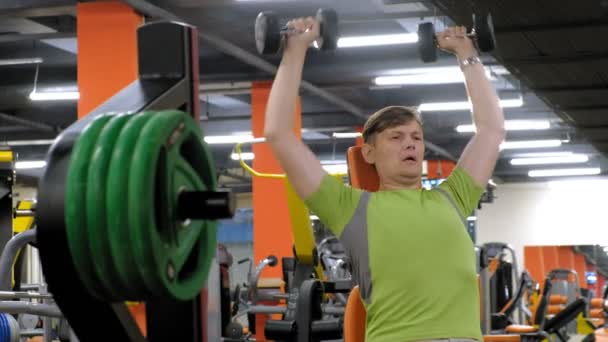 Bir adam bir fitness stüdyosunda düz bir kavrama ile oturan dumbbells ile bir bank basın yapıyor — Stok video