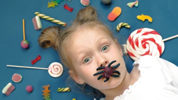 Vidám kislány fekszik a kék háttér édesség. Closeup portré — Stock videók
