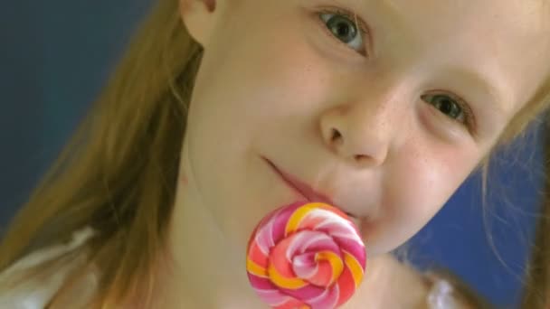 Little girl with a lollipop on a blue background. Close up portrait — Stock Video