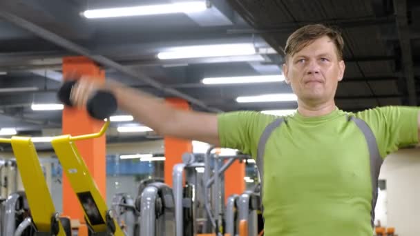 Een man doet een oefening op de rug Delta met dumbbells zittend met een rechte greep in een fitness studio — Stockvideo