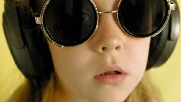 Cheerful little girl in headphones on a yellow background. Closeup portrait. — Stock Video