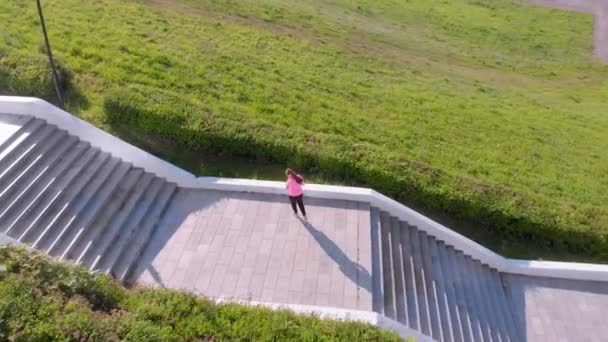 Una joven sube por las escaleras, hace deporte. Disparo aéreo — Vídeos de Stock