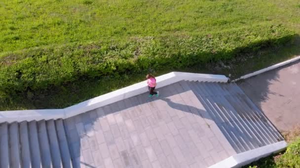 Una joven sube por las escaleras, hace deporte. Disparo aéreo — Vídeos de Stock