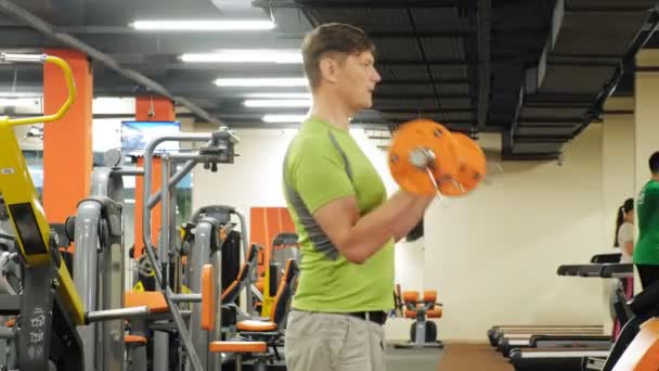 Un hombre con sobrepeso levanta una barra de ez mientras está parado en el gimnasio. Ejercicio para bíceps. Fitness. Estilo de vida saludable . — Vídeos de Stock