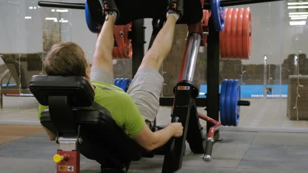Egy férfi a túlsúly csinál lábát megnyomja a szimulátor a tornateremben. Edzettségi tréning. Egészséges életmód koncepció — Stock videók