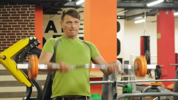 Un hombre con sobrepeso levanta una barra de ez mientras está parado en el gimnasio. Ejercicio para bíceps. Fitness. Estilo de vida saludable . — Vídeos de Stock