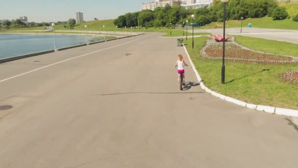 Mujer joven montando una bicicleta al aire libre en verano. Terraplén del río. Transporte ecológico. Disparo aéreo — Vídeos de Stock