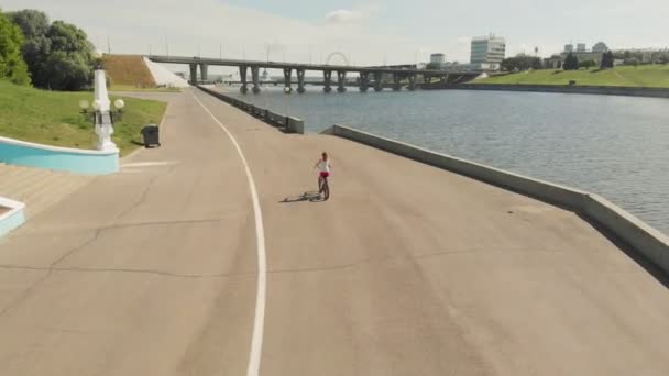 Jonge vrouw die in de zomer een fiets buitenshuis rijdt. Rivierdijk. Milieuvriendelijk vervoer. Lucht schieten — Stockvideo