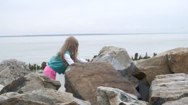 Menina pré-escolar joga em grandes pedras na costa . — Vídeo de Stock