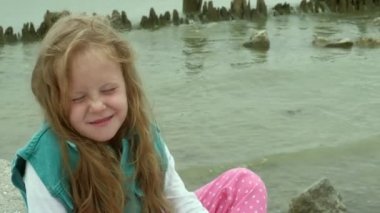 Deniz kıyısında taşlar üzerinde oturan kız çocuk.