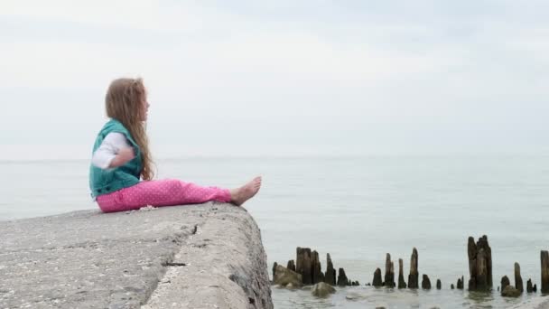 Meisje kind zittend op de stenen aan de kust. — Stockvideo
