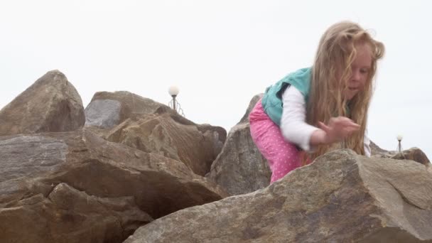 Niña preescolar juega en piedras grandes en la orilla del mar . — Vídeo de stock