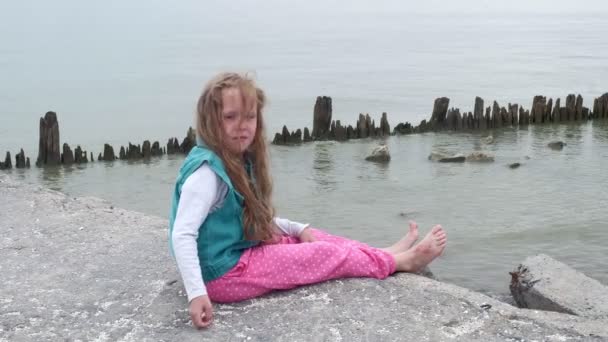 Menina criança sentada nas pedras na praia . — Vídeo de Stock