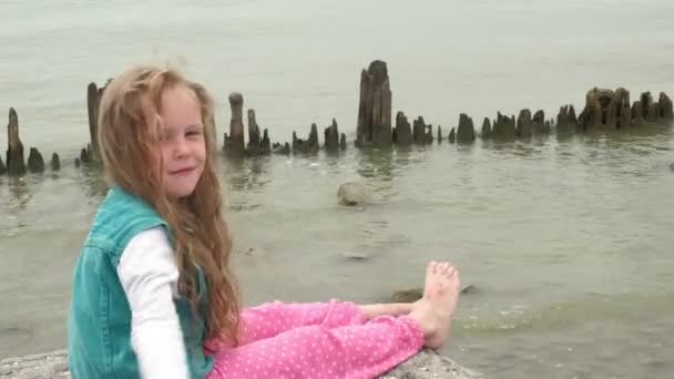 Дівчинка сидить на камені на березі моря . — стокове відео