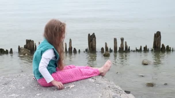 Fille enfant assis sur les pierres sur le bord de la mer . — Video
