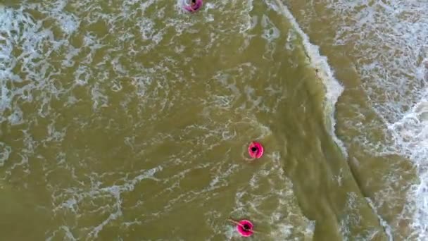 Les gens en anneaux de caoutchouc nagent sur les vagues dans la mer. Vidéo aérienne — Video