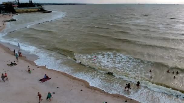 A tengerparton naplementekor. Az emberek úsznak a tengerben. Légifelvétel — Stock videók