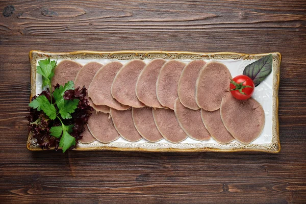 Язык говядины нарезан тонкими ломтиками на тарелке на коричневом деревенском фоне. меню ресторана — стоковое фото