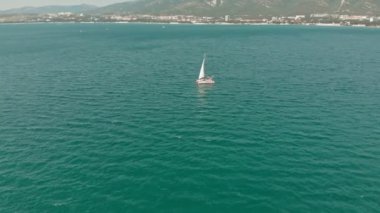 Yelkenli beyaz bir yat yazın mavi denizde yüzer. Havadan çekim