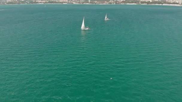 Een wit jacht met een zeil zweeft in de blauwe zee in de zomer. Luchtfoto — Stockvideo