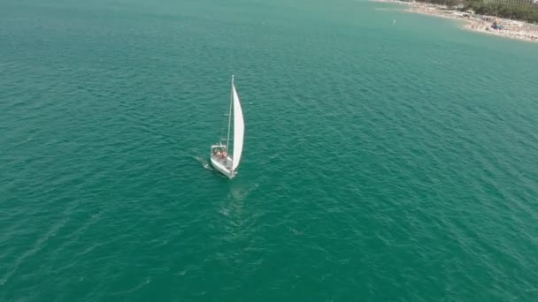 Een wit jacht met een zeil zweeft in de blauwe zee in de zomer. Luchtfoto — Stockvideo