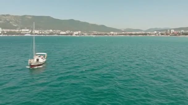 Летом в голубом море плавает белая яхта с парусом. Воздушный удар — стоковое видео