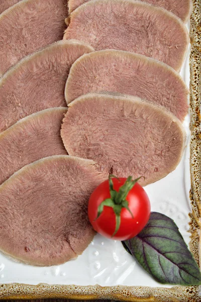 Язык говядины нарезан тонкими ломтиками на тарелке на коричневом деревенском фоне. меню ресторана — стоковое фото