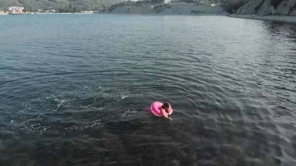 A girl floats on a rubber ring in the sea. Sea vacations in summer. Aerial shot — Stock Video