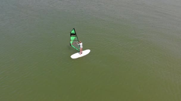 Um homem flutua numa prancha de surf com uma vela. Tiro aéreo — Vídeo de Stock