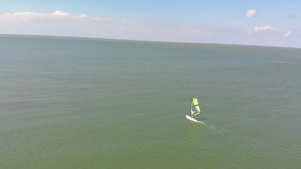 Um homem flutua numa prancha de surf com uma vela. Tiro aéreo — Vídeo de Stock