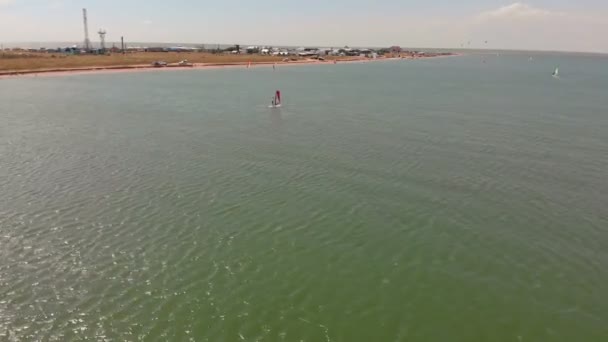 Ein Mann schwebt mit einem Segel auf einem Surfbrett. Luftaufnahme — Stockvideo