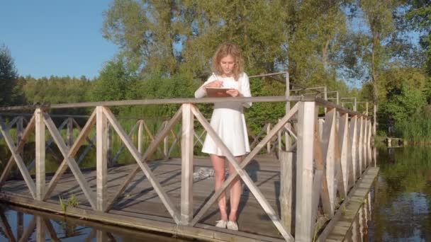 Une jeune femme utilise une tablette près de la rivière. Plan aérien — Video