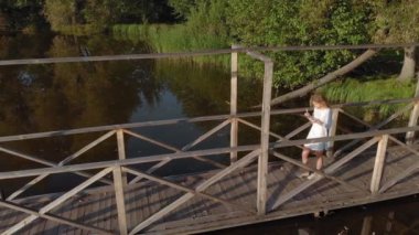 Genç bir kadın nehir kıyısında bir tablet kullanıyor. Havadan çekim