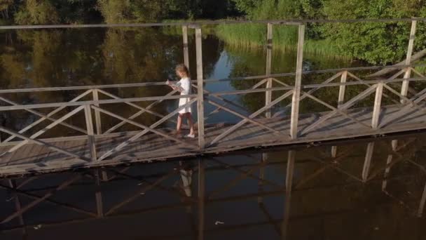 Eine junge Frau benutzt eine Tablette am Fluss. Luftaufnahme — Stockvideo