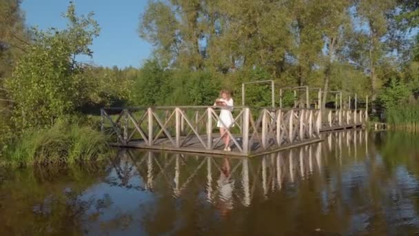 Μια νεαρή γυναίκα χρησιμοποιεί μια ταμπλέτα δίπλα στο ποτάμι. Εναέρια βολή — Αρχείο Βίντεο