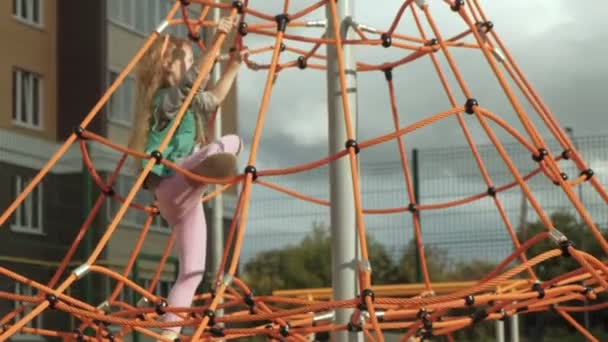 Bir çocuk açık bir oyun alanında bir ip yatay bar tırmanıyor — Stok video