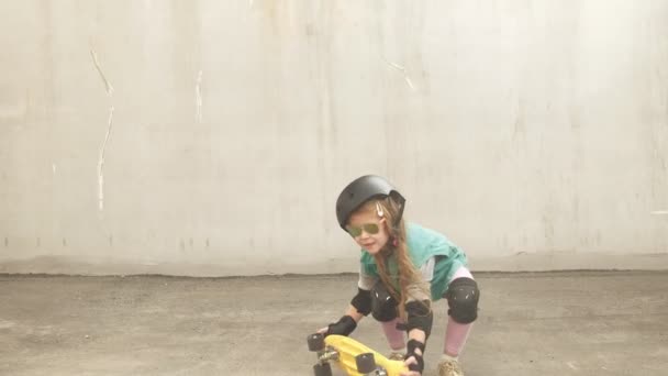 En liten flicka rider på en gul skateboard — Stockvideo