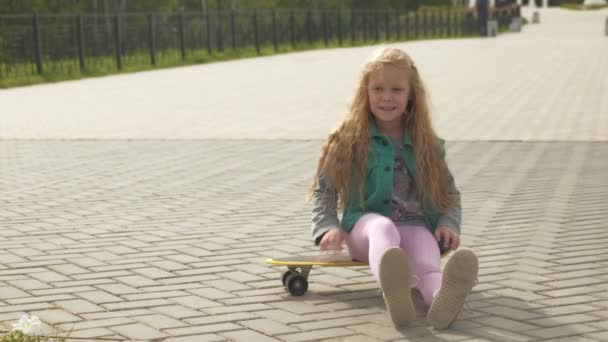 Une petite fille monte sur une planche à roulettes jaune — Video